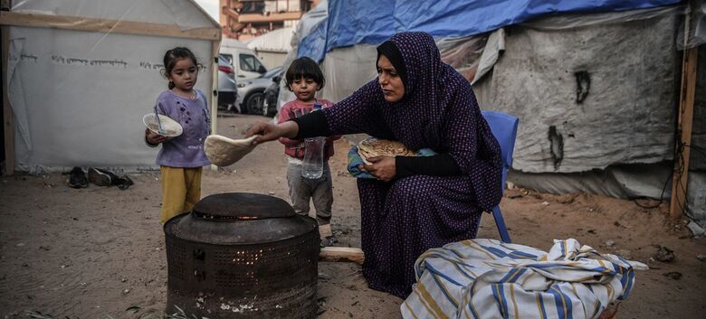 Uma mãe prepara uma refeição para seus filhos do lado de fora de sua casa improvisada em um campo de refugiados em Khan Younis, Gaza - Crédito:  Unicef/Abed Zagout 